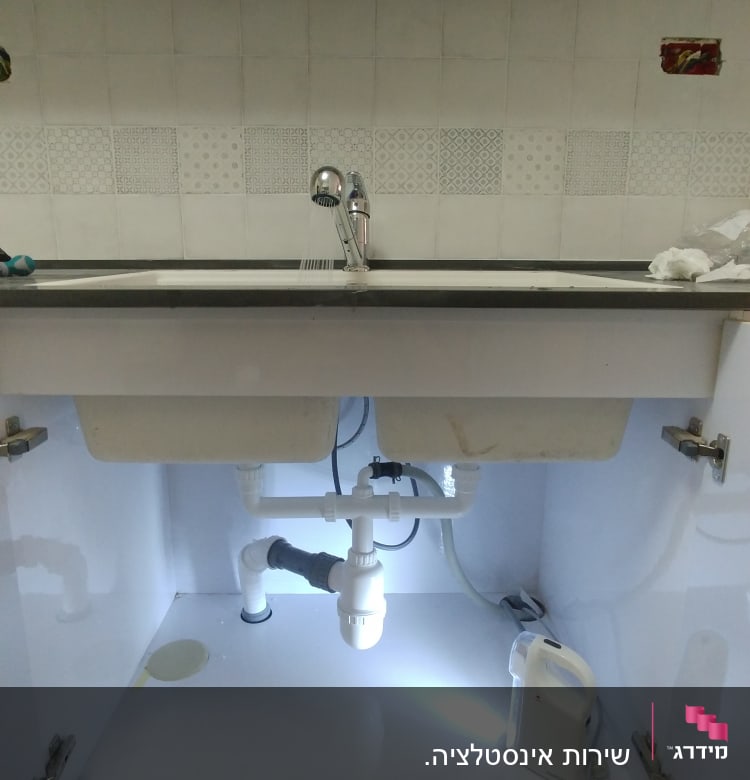 כיור מטבח עם צנרת ותאורה מתחת לארון